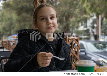 Pretty young child girl drinking coffee and eating croissant in city street cafe 125689335