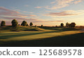 A tranquil golf course landscape captured during sunset, showcasing smooth rolling greens, tree clusters, and a pastel-colored sky. 125689578