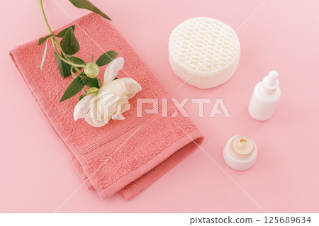 Towel with a peony flower and body care products on the pink background. Towel with a peony flower and body care products on the pink background. 125689634