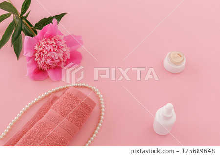 Towel with body care products and a peony flower on the pink background. Towel with body care products and a peony flower on the pink background. 125689648