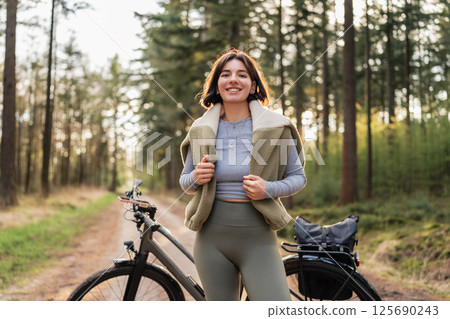 Young woman biking under tall trees, linking mindful movement, seasonal escape, and sport-infused travel 125690243