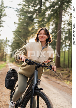 Fit traveler rides a bike along wooded paths, where cycling meets wellness and warm-weather adventure vibes 125690246