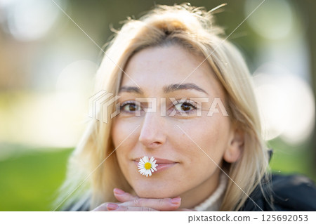 Blonde woman holding a daisy in her mouth in a park 125692053