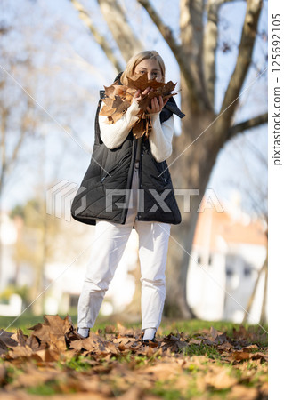 Young woman holding autumn leaves in a park 125692105
