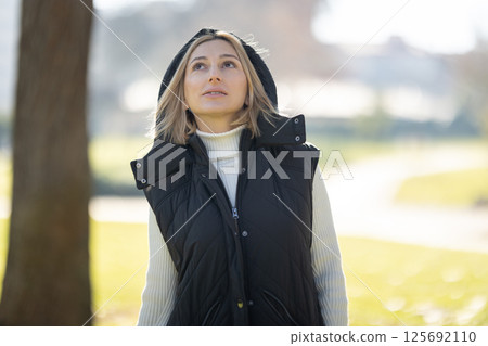 Woman wearing vest and looking up in a park during a sunny day 125692110