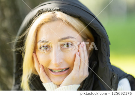 Blonde woman wearing braces and holding her face with hands 125692176