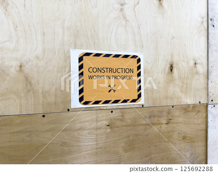 Urban plywood wall with printed construction warning sign, minimalist industrial style element, signage detail from building site, modern city infrastructure and architecture background Urban plywood wall with printed construction warning sign, minimalist industrial style element, signage detail from building site, modern city infrastructure and architecture background 125692288