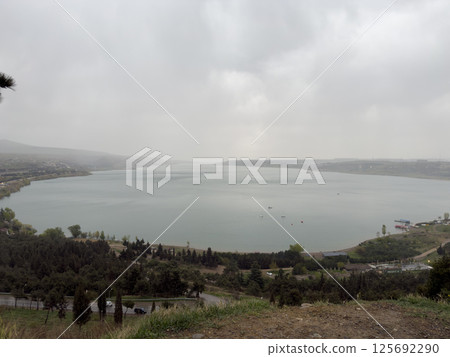 Overcast panoramic view of Tbilisi Sea reservoir with calm water and cloudy sky, surrounded by forest and hills. Scenic nature landscape with moody weather and urban edge in Georgia Overcast panoramic view of Tbilisi Sea reservoir with calm water and cloudy sky, surrounded by forest and hills. Scenic nature landscape with moody weather and urban edge in Georgia 125692290