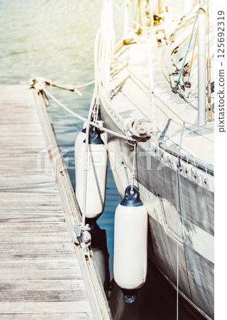 Sailboat docked at marina with sunlight, water reflection, wooden pier background Sailboat docked at marina with sunlight, water reflection, wooden pier background 125692319