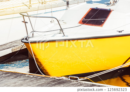 Yellow sailboat moored at marina dock with sunlit reflections, background 125692323