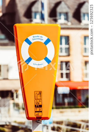Life buoy in bright orange container by quaint buildings, safety concept Life buoy in bright orange container by quaint buildings, safety concept 125692325
