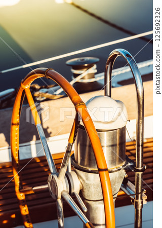 Sailboat steering wheel and rigging lit by warm sunlight, perfect for nautical themes Sailboat steering wheel and rigging lit by warm sunlight, perfect for nautical themes 125692326