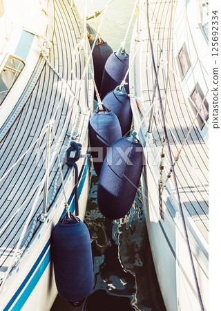Sailboats with protective fenders anchored at marina, sunlight creating reflections 125692334