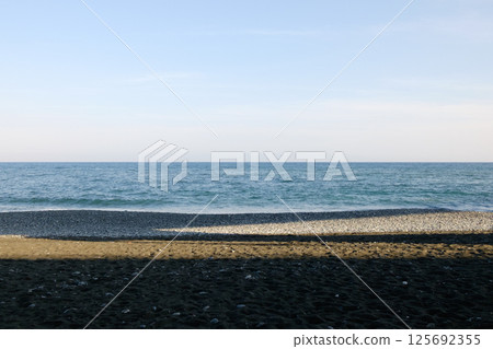 White waves crashing on a sandy beach under the hazy blue spring sky and deep sunlight White waves crashing on a sandy beach under the hazy blue spring sky and deep sunlight 125692355
