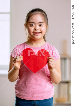 Young Girl Holds Red Heart Cutout in a Bright Room During a Joyful Moment 125692683