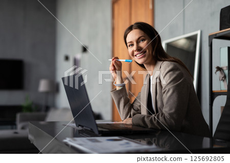 Professional woman working in office. She is seated at desk with a laptop and documents. 125692805