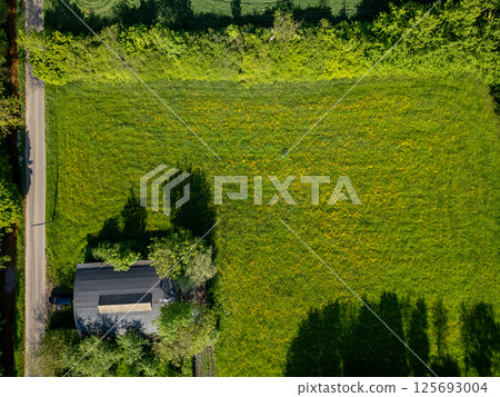 Aerial View of a Lush Green Field Surrounded by a House and Abundant Trees in Nature Aerial View of a Lush Green Field Surrounded by a House and Abundant Trees in Nature 125693004