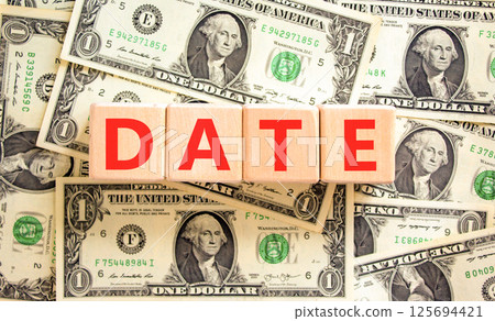 Date symbol. Concept word Date on beautiful wooden blocks. Dollar bills. Beautiful background from dollar bills. Business and date concept. Copy space. 125694421