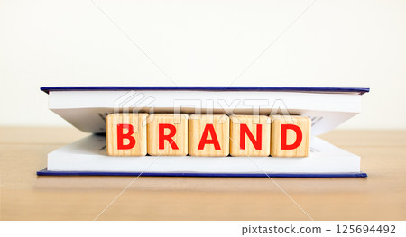 Brand symbol. Concept word Brand on beautiful wooden blocks in book. Beautiful wooden table white background. Business brand concept. Copy space. Brand symbol. Concept word Brand on beautiful wooden blocks in book. Beautiful wooden table white background. Business brand concept. Copy space. 125694492