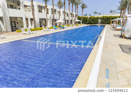 Summer seaside relax mood travel vacation a luxurious pool hotel interior for a summer holiday in warm countries. Beautiful tropical beach hotel resort with swimming pool, sun loungers palm trees 125694612