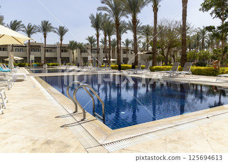 Summer seaside relax mood travel vacation a luxurious pool hotel interior for a summer holiday in warm countries. Beautiful tropical beach hotel resort with swimming pool, sun loungers palm trees 125694613
