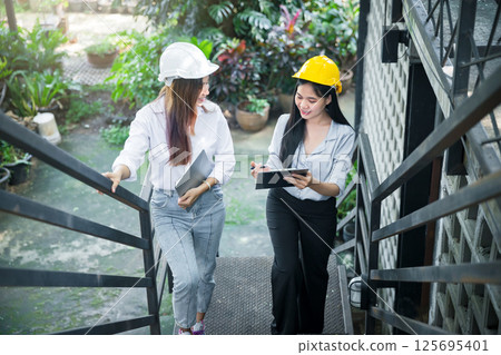 Two young female architects chatting as they walk up the stairs. 125695401