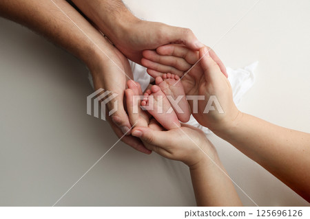 A father and mother hold the feet of a newborn child in a white blanket on a white background.. The feet of a newborn in the hands of parents. Photo of foot, heels and toes.The palms of the parents. A father and mother hold the feet of a newborn child in a white blanket on a white background.. The feet of a newborn in the hands of parents. Photo of foot, heels and toes.The palms of the parents. 125696126