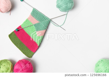 Striped piece of knitted fabric for future clothing with knitting needles and balls of thread on gray background. Homemade needlework and knitting of warm, clothes and toys. Concept creativity Striped piece of knitted fabric for future clothing with knitting needles and balls of thread on gray background. Homemade needlework and knitting of warm, clothes and toys. Concept creativity 125696166