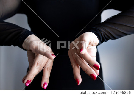 Caucasian female hands with red nails in artistic pose wearing black long sleeve attire 125696896