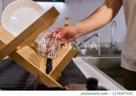 Carefully hand placing a clean, sparkling dish into the drying rack for organization and hygiene Carefully hand placing a clean, sparkling dish into the drying rack for organization and hygiene 125697585