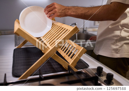 Carefully hand placing a clean, sparkling dish into the drying rack for organization and hygiene 125697588