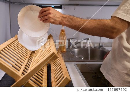 Carefully hand placing a clean, sparkling dish into the drying rack for organization and hygiene 125697592