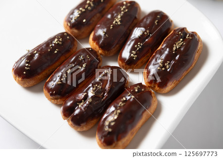 Eight classic eclairs arranged neatly on a white plate. 125697773