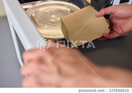 Hand delicately placing a takeout container into the microwave to warm up the meal 125698020
