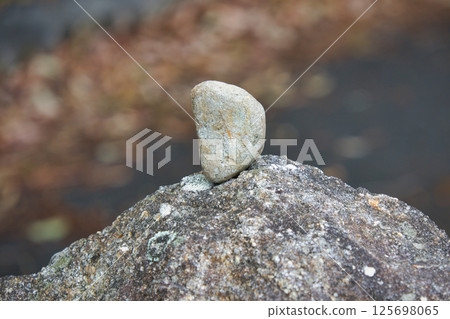 A small pebble balanced on a large rock 125698065