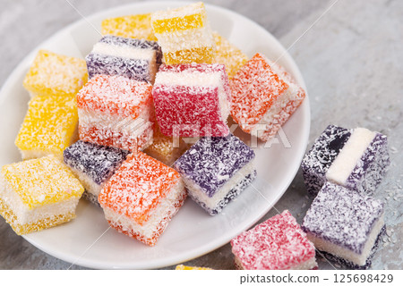 Cubes of multi-colored marmalade in powdered sugar on plate. The concept of baby sweets. 125698429