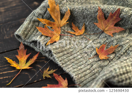 Autumn composition. Knitted plaid or scarf and fallen leaves on dark grey background. Hello Autumn, Cozy atmosphere. Flat lay, copy space. Autumn composition. Knitted plaid or scarf and fallen leaves on dark grey background. Hello Autumn, Cozy atmosphere. Flat lay, copy space. 125698430