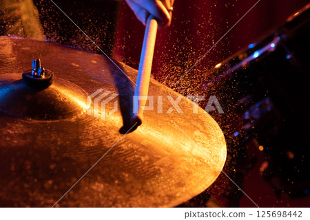 Drum sticks hitting snare drum with splashing water on dark background with orange and blue studio lighting. Dynamic scene 125698442