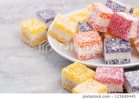 Cubes of multi-colored marmalade in powdered sugar on plate. The concept of baby sweets. Cubes of multi-colored marmalade in powdered sugar on plate. The concept of baby sweets. 125698445