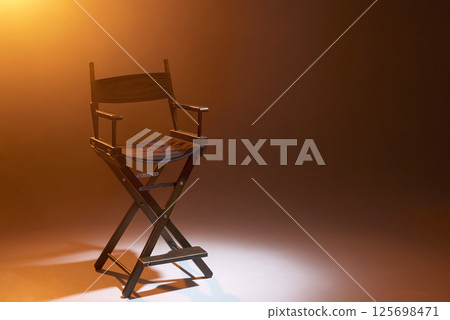 The director's chair stands in a beam of light with an orange backlight and smoke. Place for text. Free chair. Concept of selection and casting. Shadow and light. 125698471