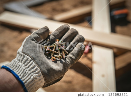 Construction worker holding screws in gloved hand on building site Construction worker holding screws in gloved hand on building site 125698851