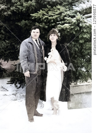 Vintage portrait of the bride and groom in a snowfall against the background of snow-covered fir trees. Retro photo from 1993. Vintage portrait of the bride and groom in a snowfall against the background of snow-covered fir trees. Retro photo from 1993. 125698877
