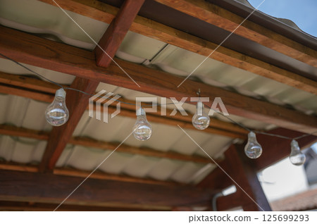 Light bulbs hanging from wooden beams under a roof 125699293