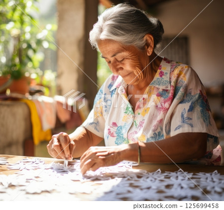 An elderly woman meticulously assembles delicate, white paper cutouts, showcasing traditional craftsmanship 125699458