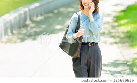 Smiling woman/businesswoman talking on her smartphone while walking along the promenade 125699639