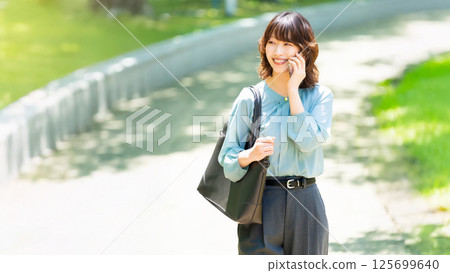 微笑的女人/女商人在海濱長廊散步時用智慧型手機聊天 125699640