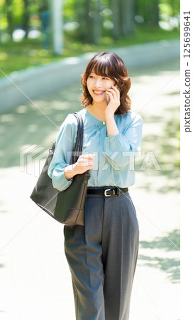 微笑的女人/女商人在海濱長廊散步時用智慧型手機聊天 125699641