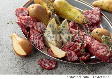 Blue cheese, dry-cured sausages, thyme and pears on a stone table. Blue cheese, dry-cured sausages, thyme and pears on a stone table. 125699853