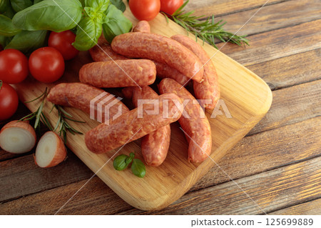 Sausages with basil and tomatoes on a cutting board. 125699889