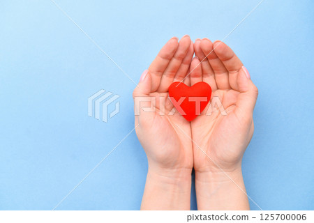 Red symbol heart in hands on a blue background. The concept of Valentine's Day and Women's Day. Top view, place for text. a life. 125700006